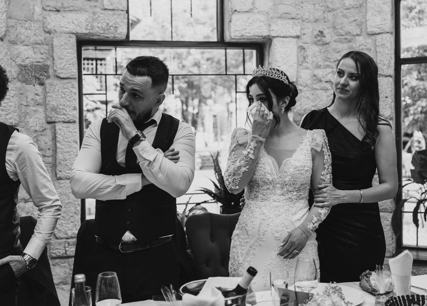Bride and groom sharing emotional moment with bridesmaid at reception.