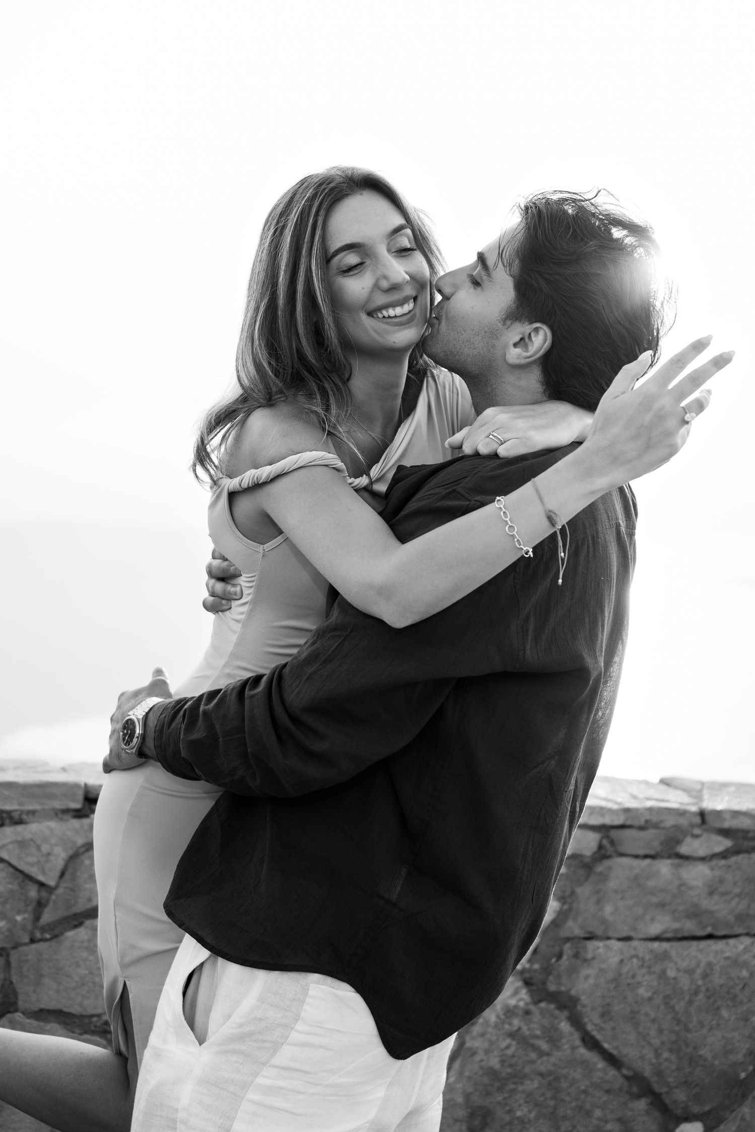 Black and white photo of a joyful couple embracing and laughing at a scenic overlook.