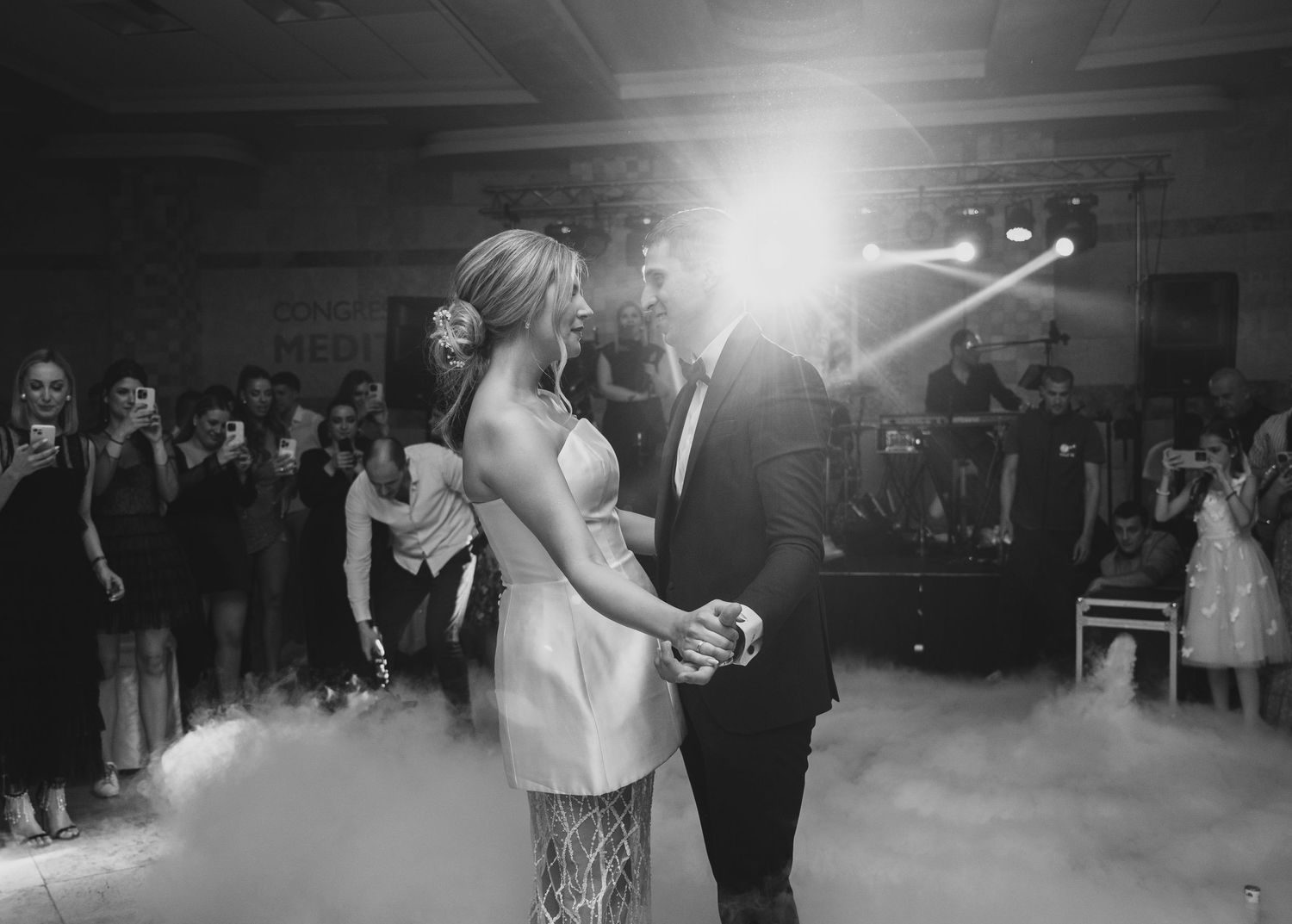 Bride and groom share first dance surrounded by fog machine effects and stage lighting at wedding reception.