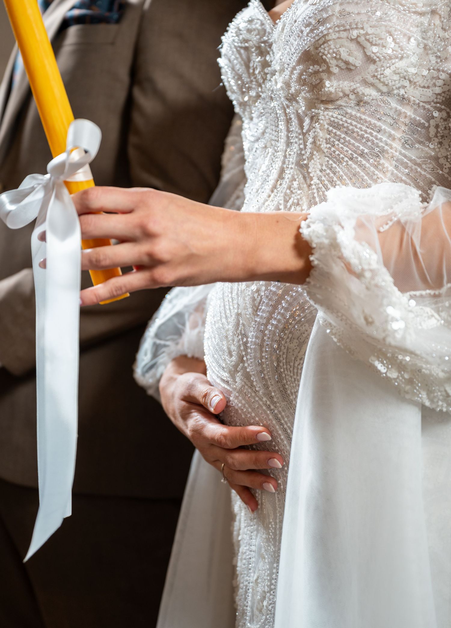 Close-up of bride in beaded lace gown holding yellow unity candle with white ribbon.