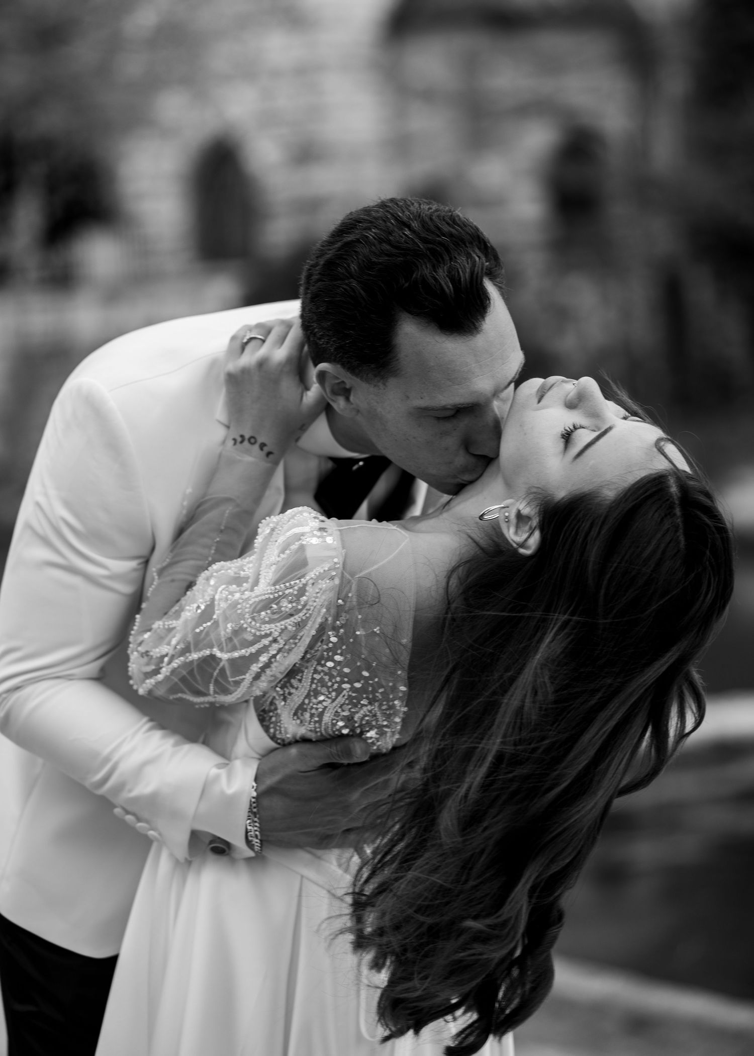 Black and white photo of a couple sharing a romantic kiss, the bride leaning back in her groom's arms.