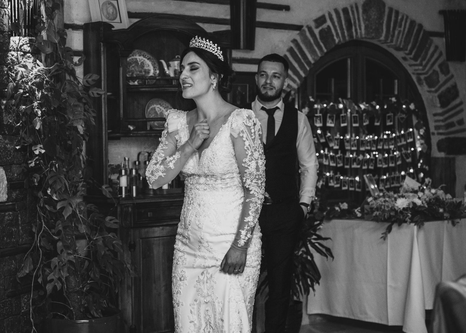 Bride in lace gown and tiara standing with groomsman at wedding.
