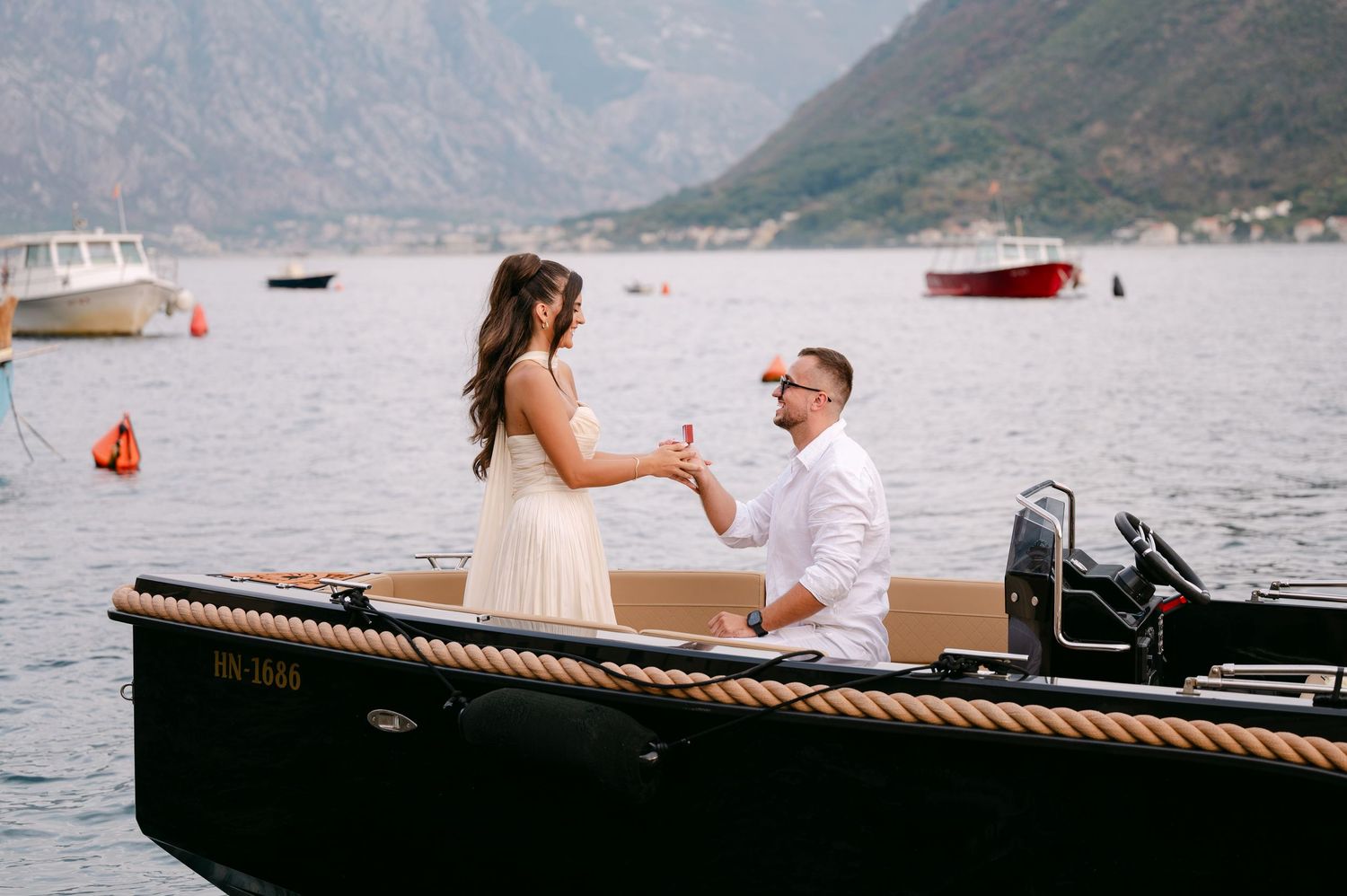Couple celebrates engagement with champagne on black boat in scenic Bay of Kotor Montenegro.