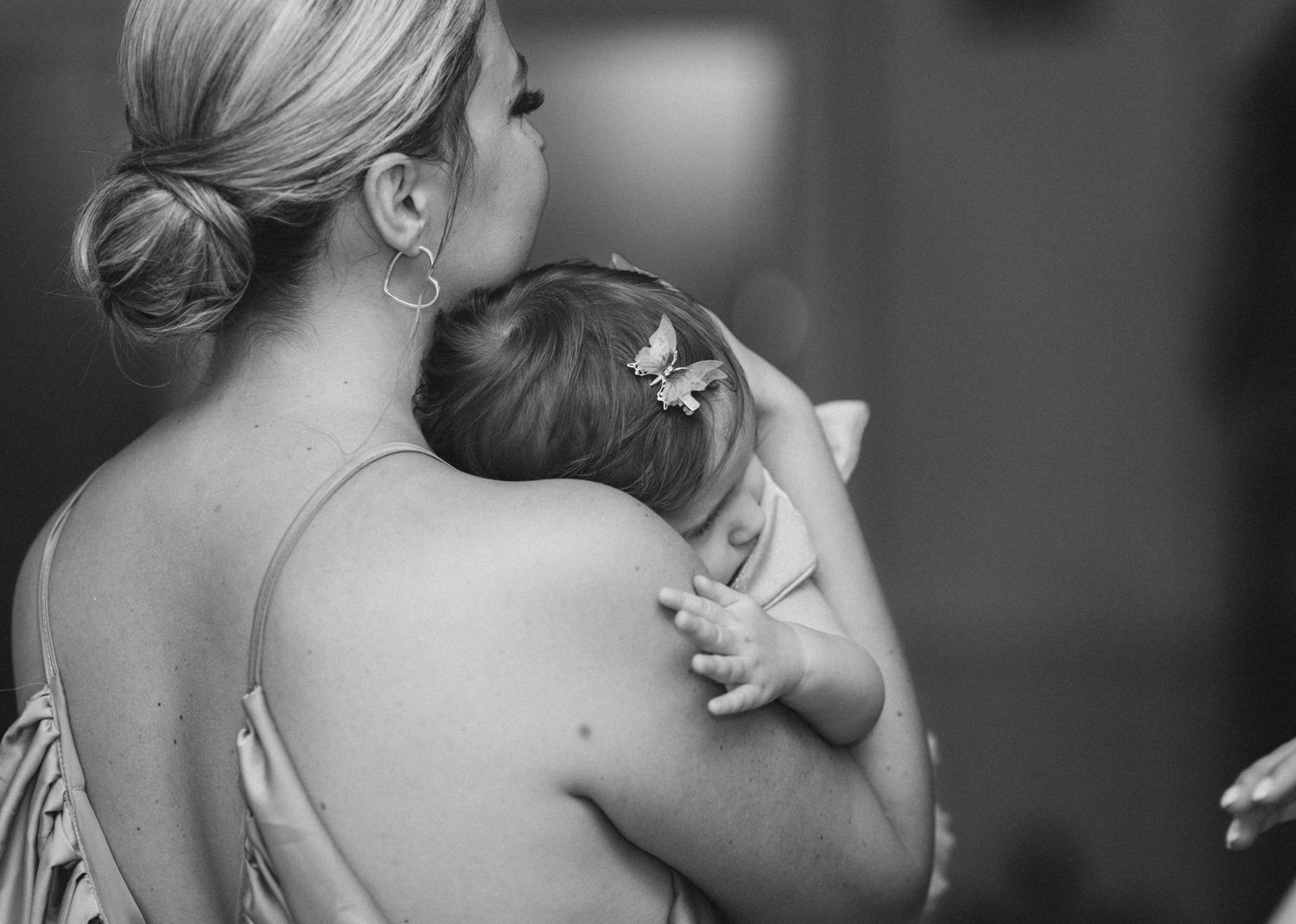 Black and white photo of a woman holding a sleeping baby with a butterfly hair clip.