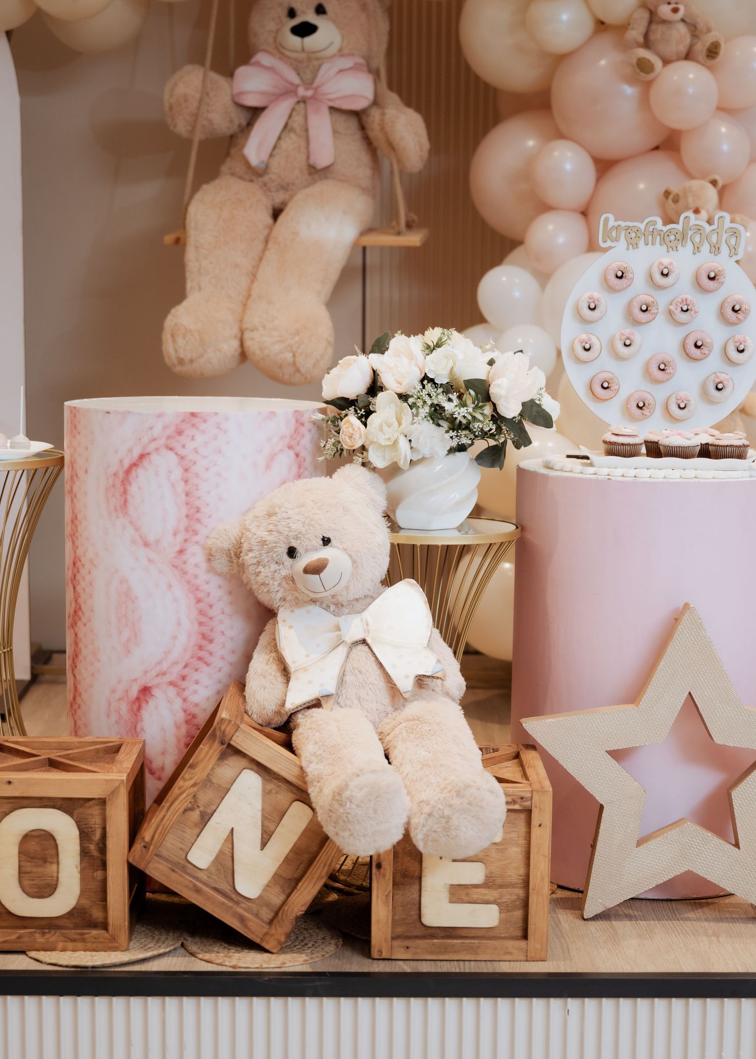 Teddy bear on ONE blocks with pink cylinder cakes, star decor, and balloon garland backdrop.