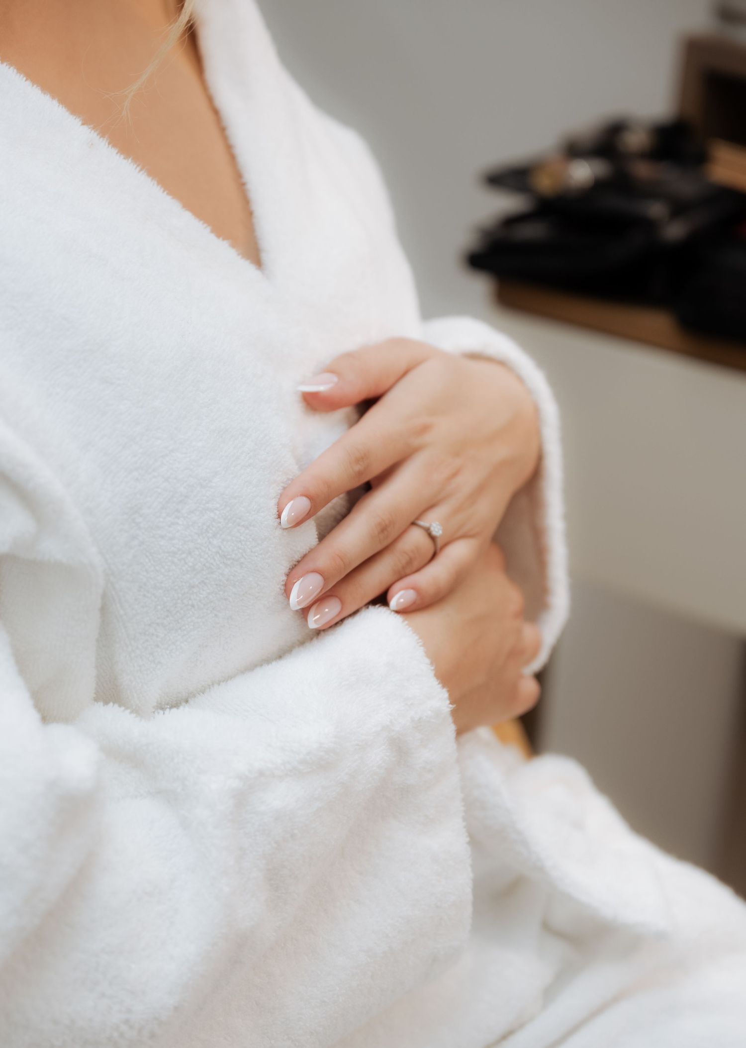 Bride in white fluffy robe with elegant French manicure and diamond engagement ring getting ready.
