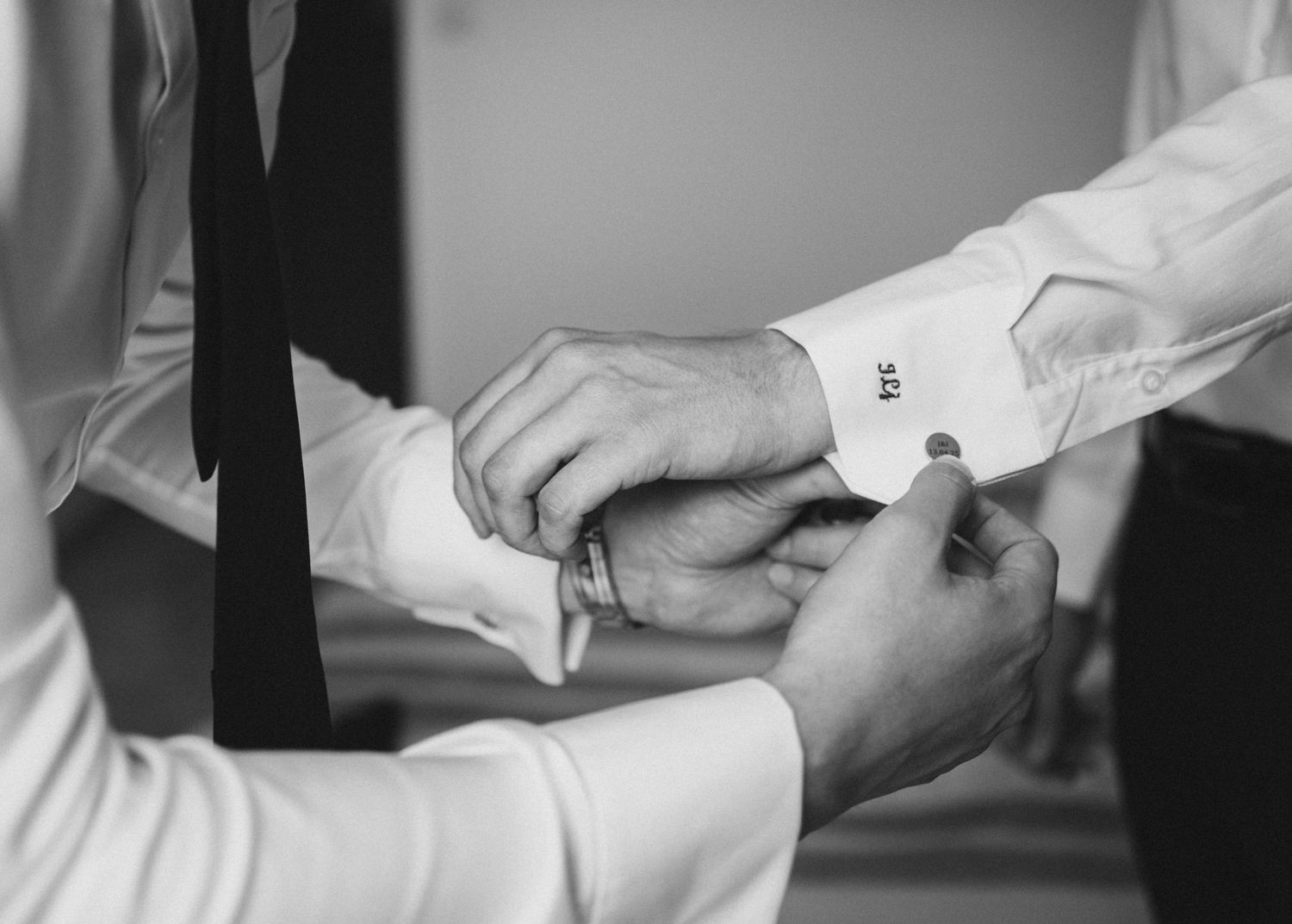 Black and white close-up of a groomsman fastening cufflinks on the groom's dress shirt.