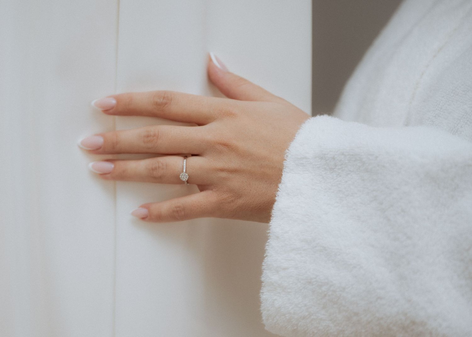 Close-up of a bride's hand wearing an engagement ring while wearing a white robe.