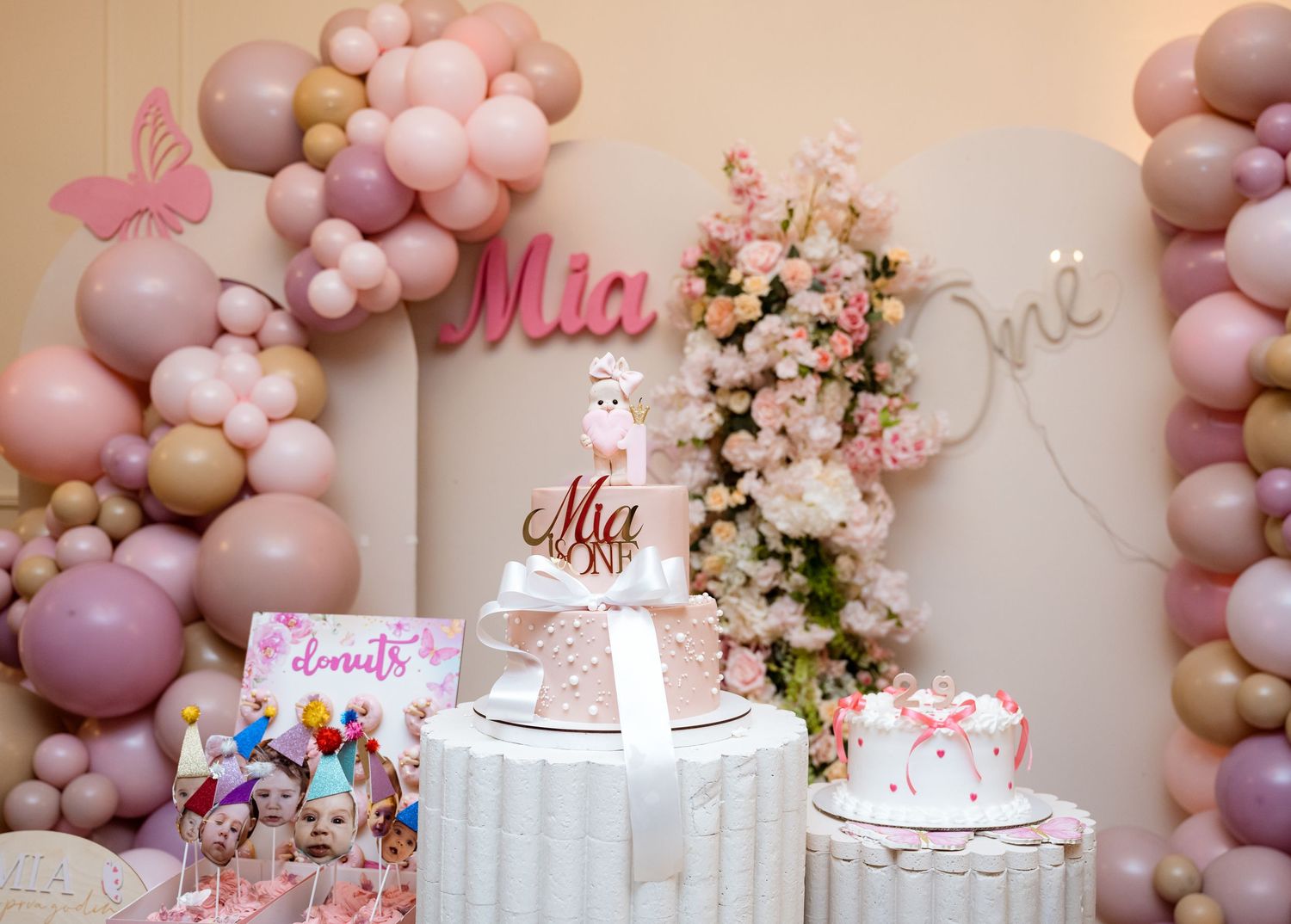 Elegant pink balloon arch birthday party setup with floral backdrop for baby Mia's first birthday.