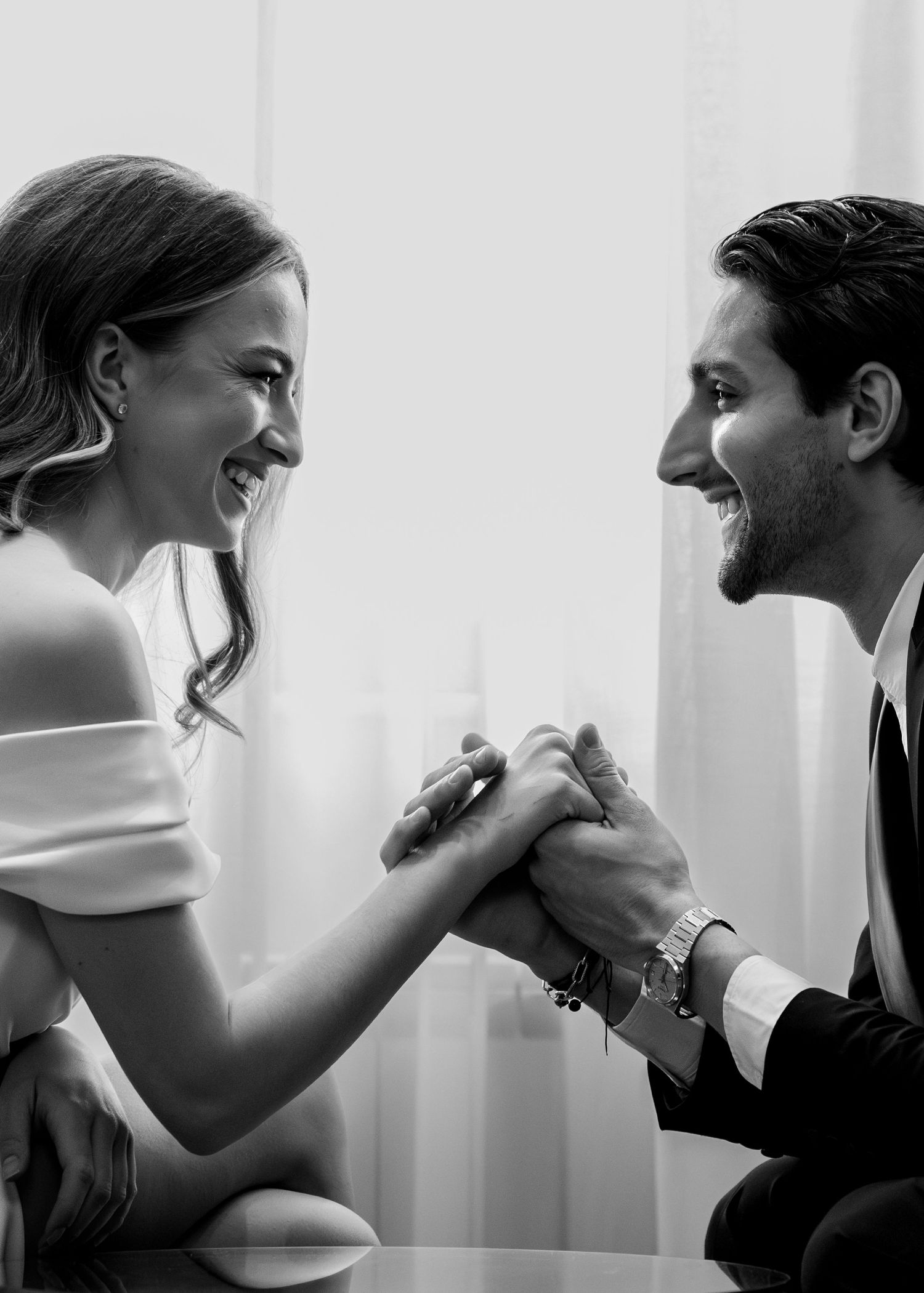 Laughing bride and groom hold hands joyfully in bright black and white wedding portrait.
