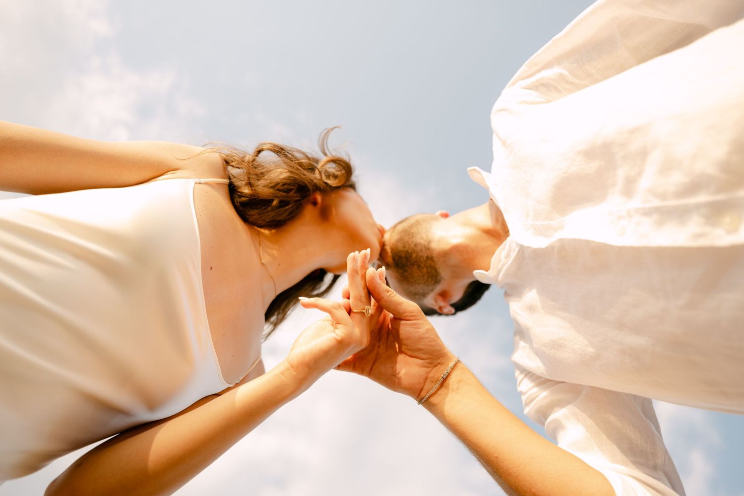 Low angle view of couple holding hands against bright blue sky in white summer outfits.
