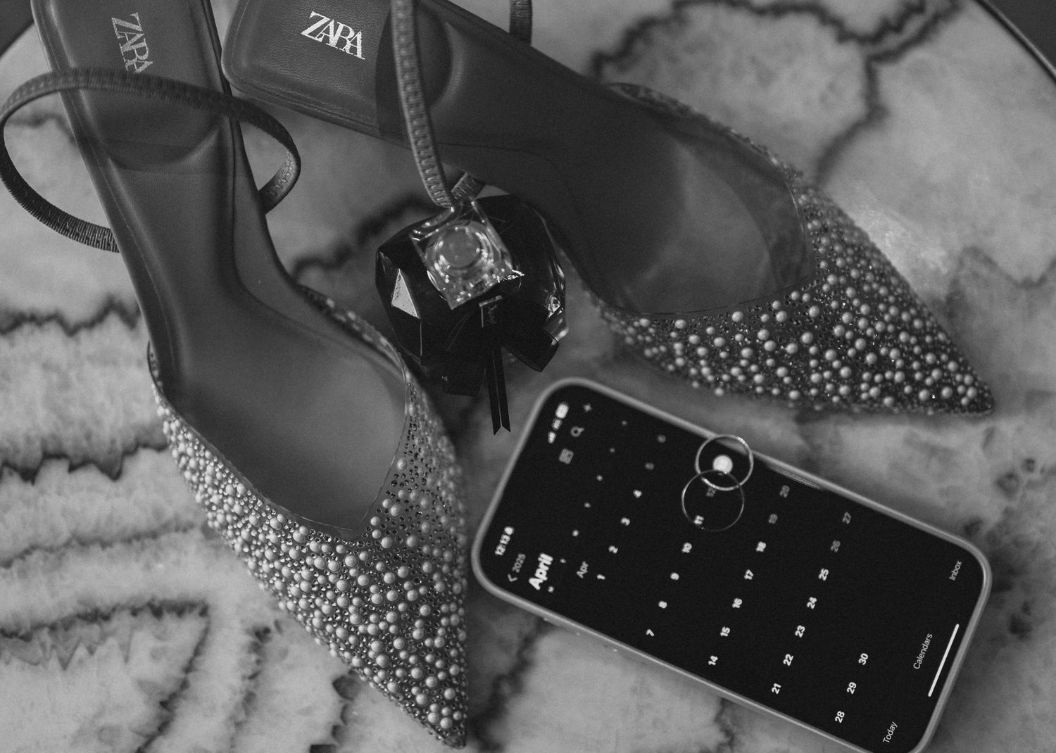 Sparkly Zara heels next to perfume bottle and smartphone on textured surface.