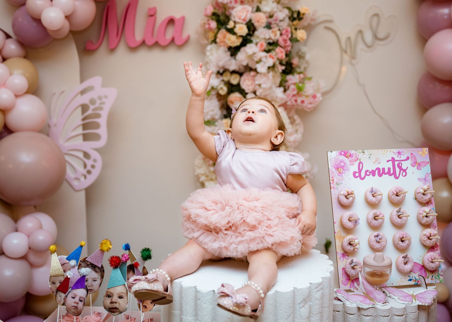 Baby girl in pink tutu dress reaching up at her Mia One first birthday party.