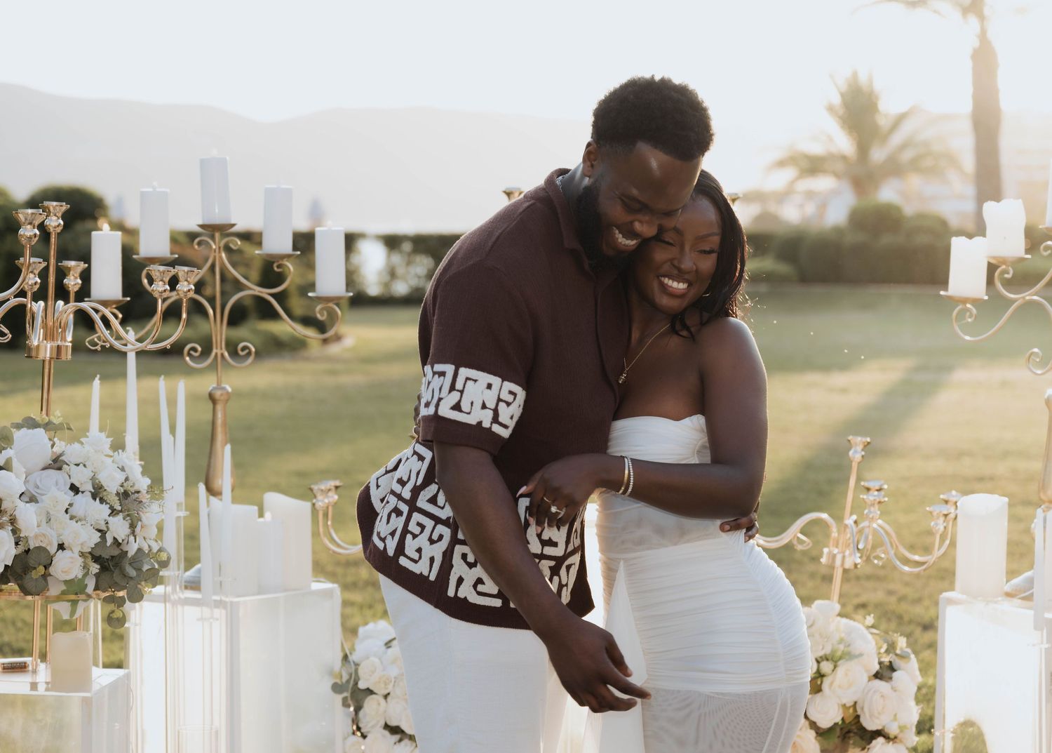 A joyful couple celebrating their engagement surrounded by candles and white floral arrangements.