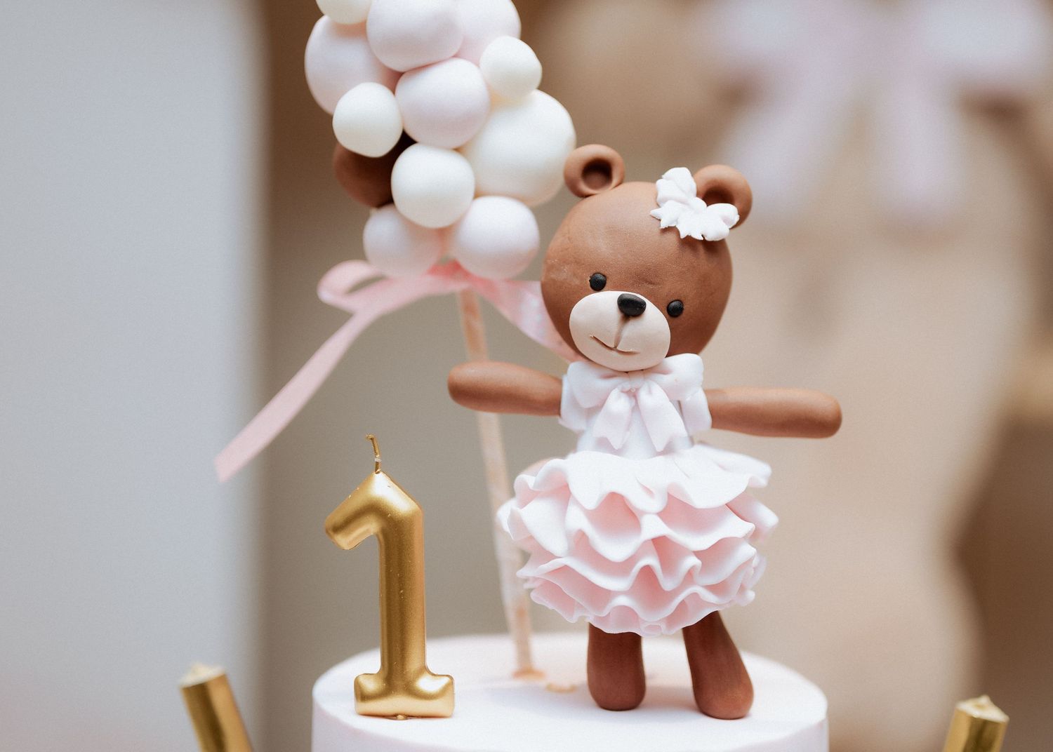 Close-up of a fondant teddy bear in a pink dress with balloons on a first birthday cake topper.