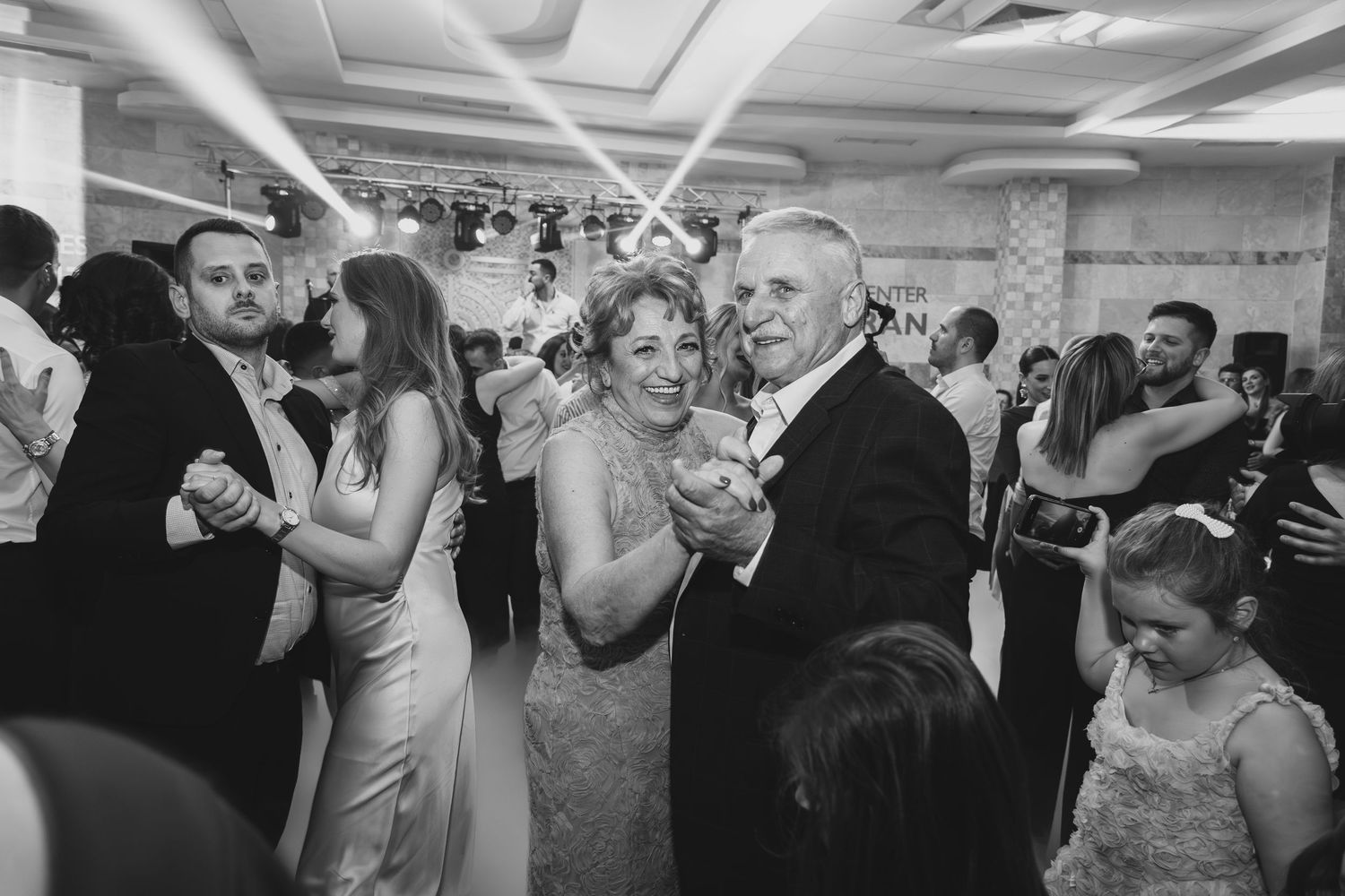 Bride dancing with older man at wedding reception while guests celebrate around them.
