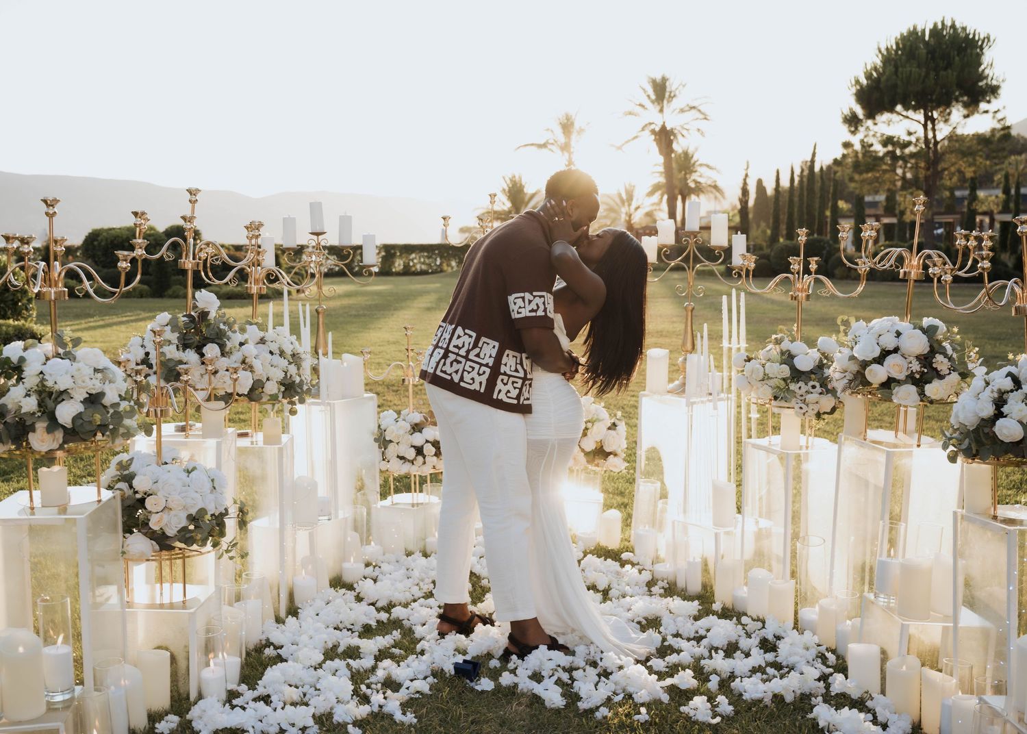 Couple embracing surrounded by white flowers and tall candles in romantic outdoor wedding setting.