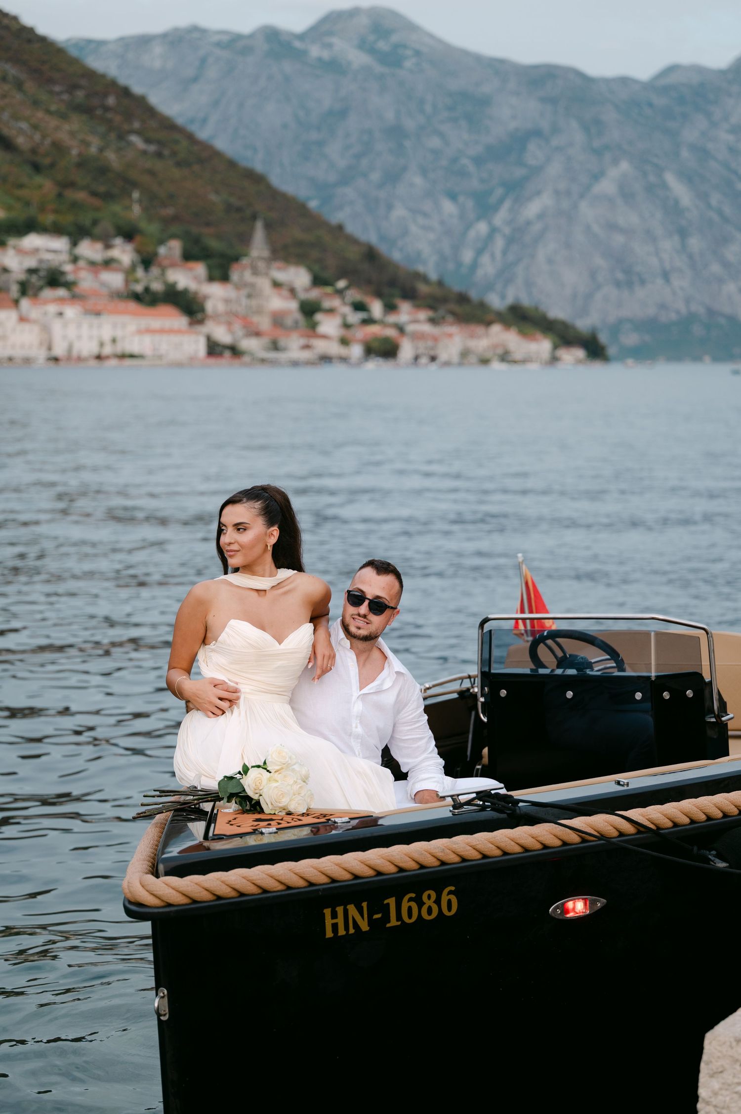 Bride and groom sitting on a luxury boat HN-1686 with scenic Bay of Kotor Montenegro mountains backdrop.