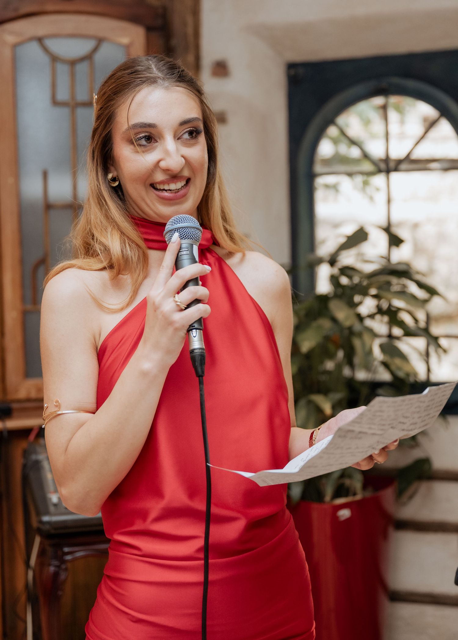 Smiling woman in red halter dress giving speech with microphone.