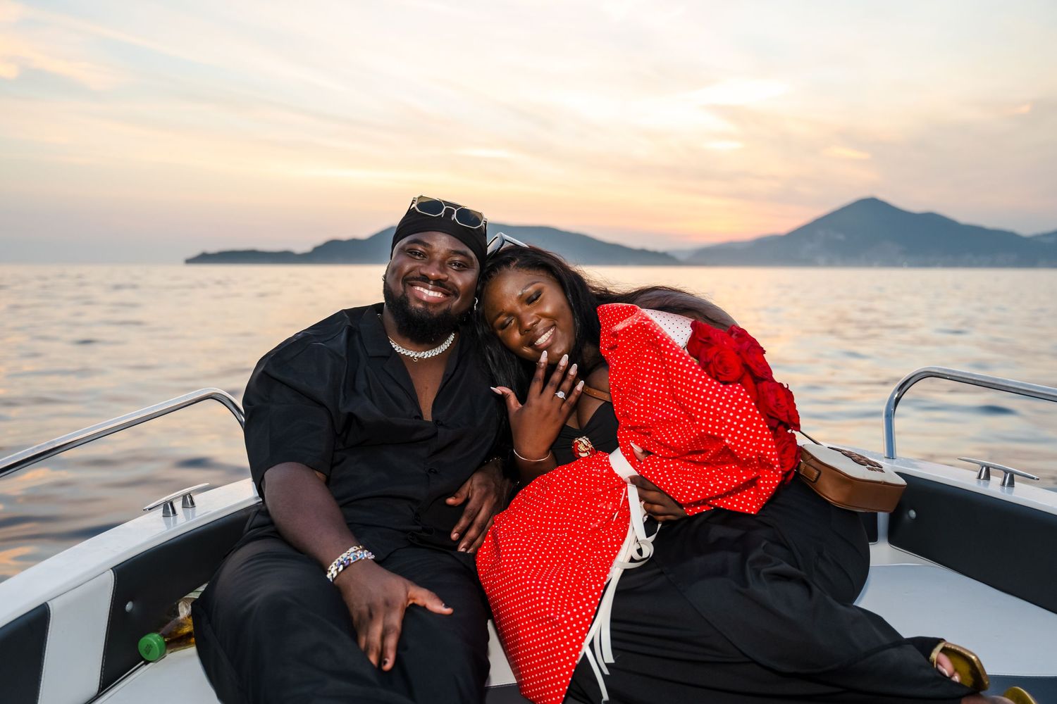 Couple sitting together on a boat at sunset with mountains and calm water in the background.