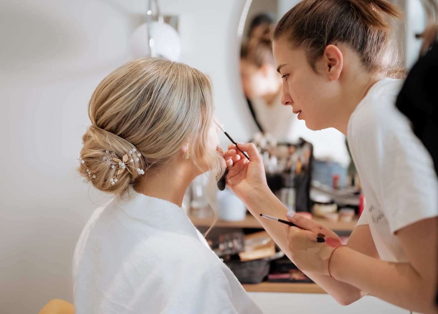 Makeup artist applying eyeshadow to blonde bride with elegant updo before wedding.