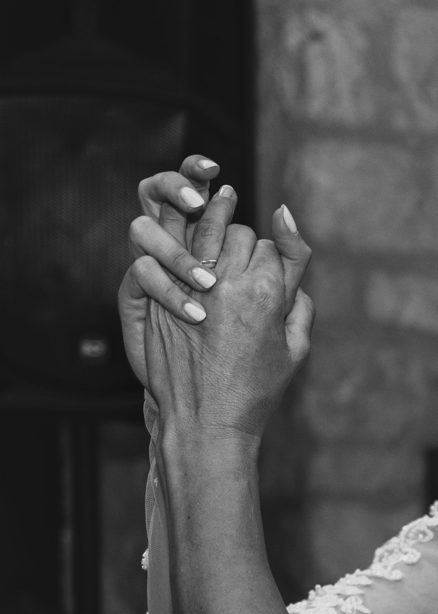Close-up black and white photo of bride and groom holding hands showing engagement ring.