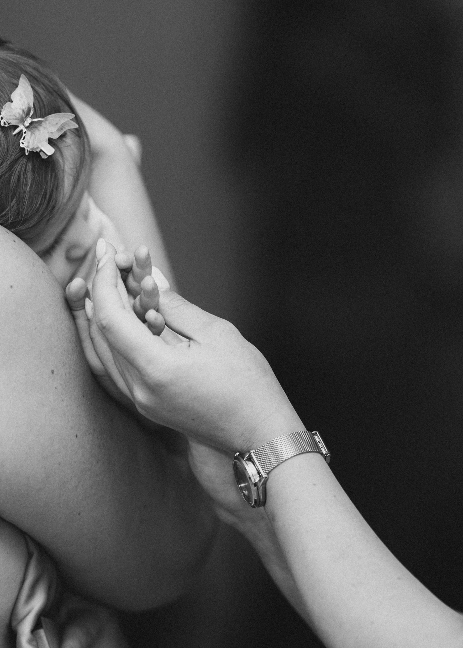 Close-up black and white photo of hands holding a baby with a butterfly hair clip.