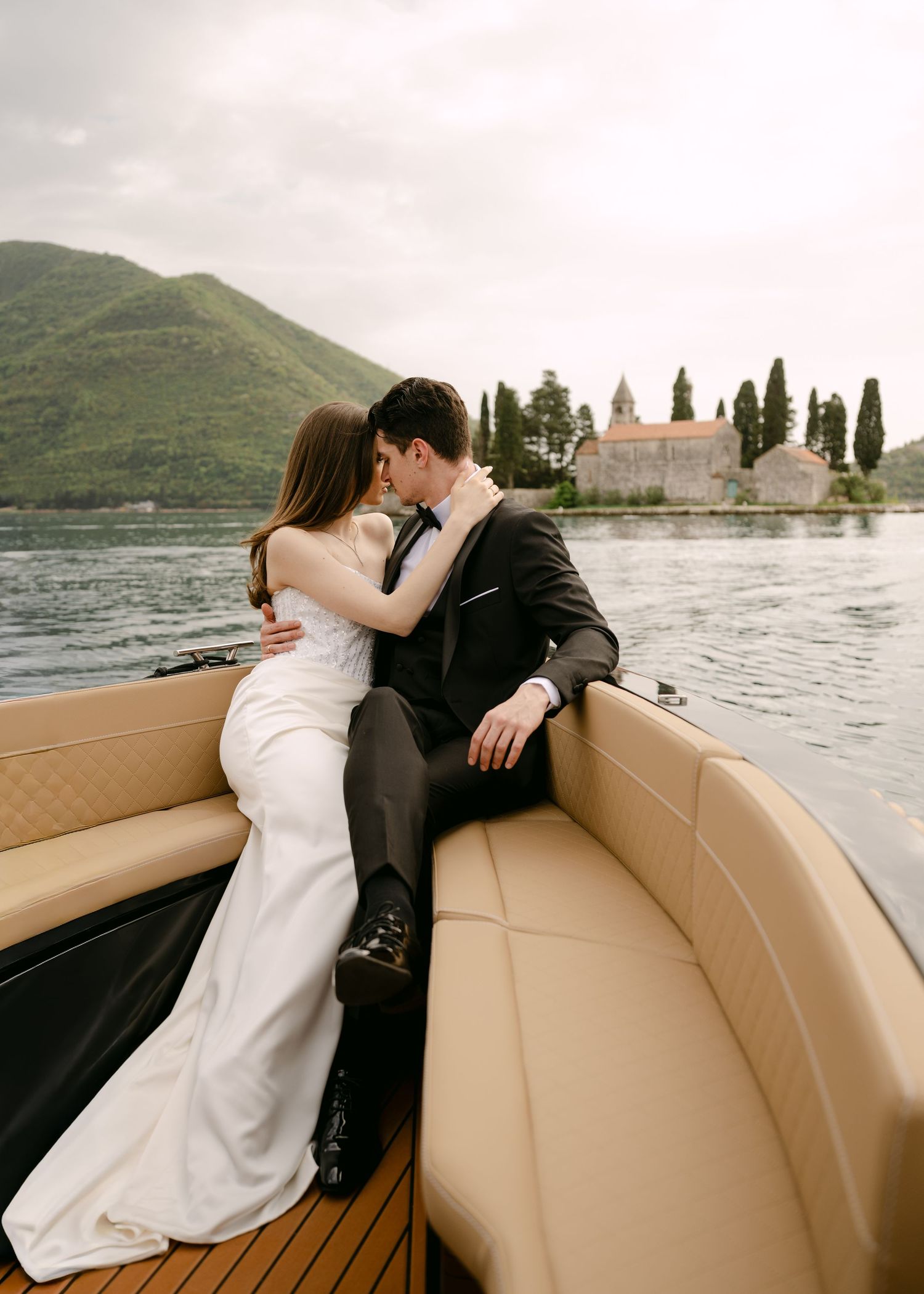 Wedding couple sharing a kiss on an elegant boat with the historic St. George Island visible in the background.