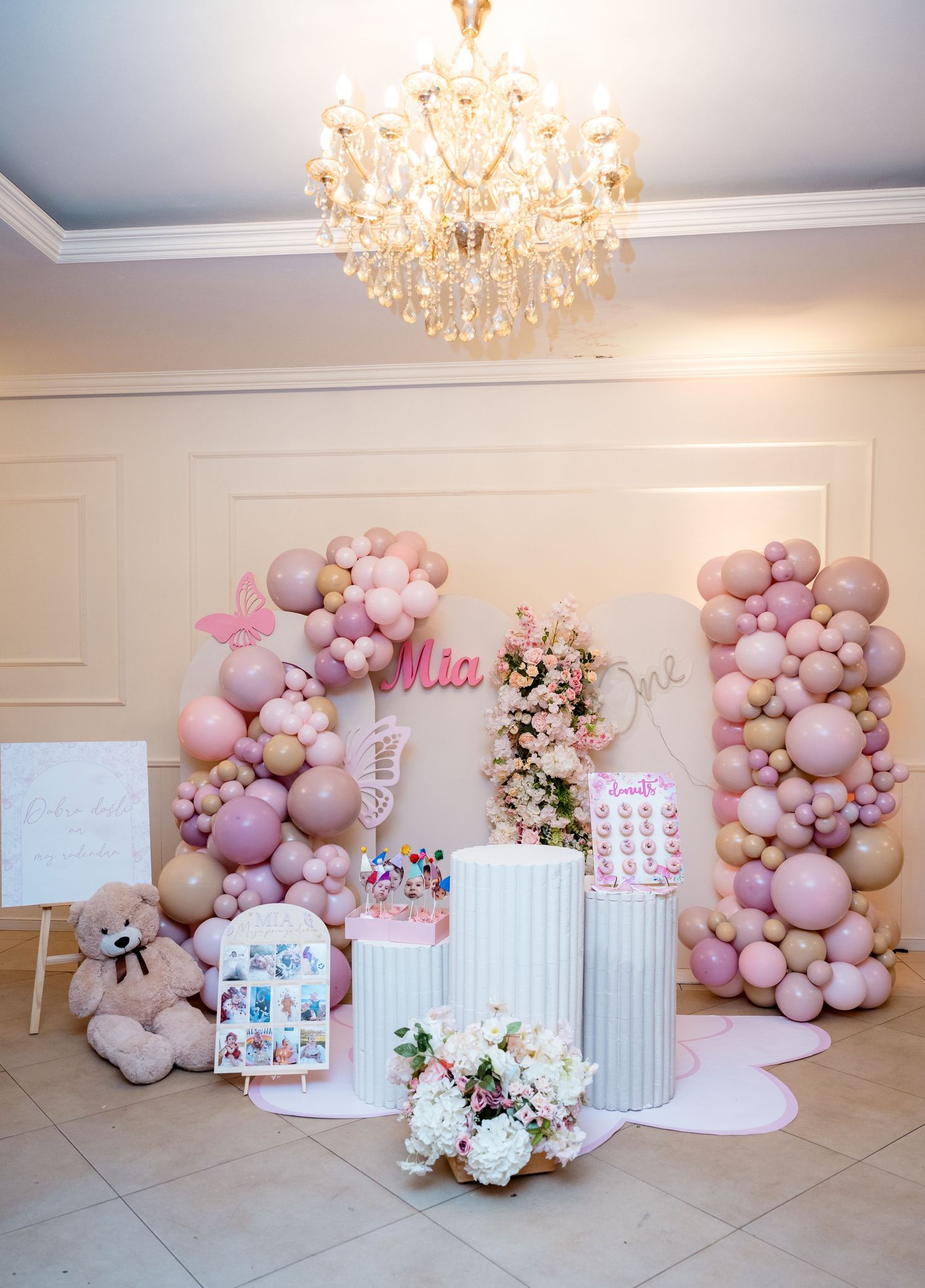 Elegant pink and gold first birthday party decoration with balloon arch and chandelier.