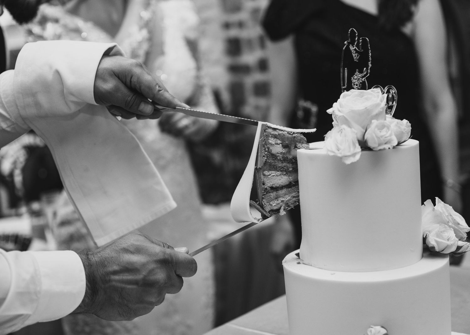 Bride and groom cutting white wedding cake with floral topper.