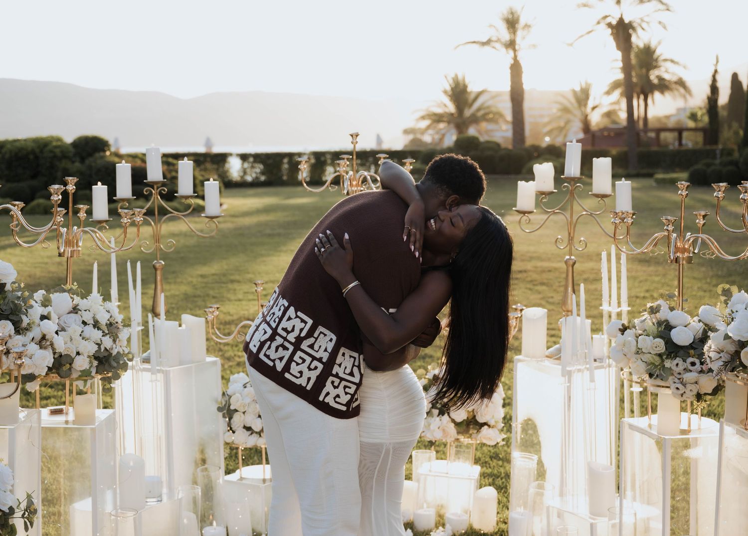 An engaged couple sharing a heartfelt embrace among candles and flowers after a proposal.