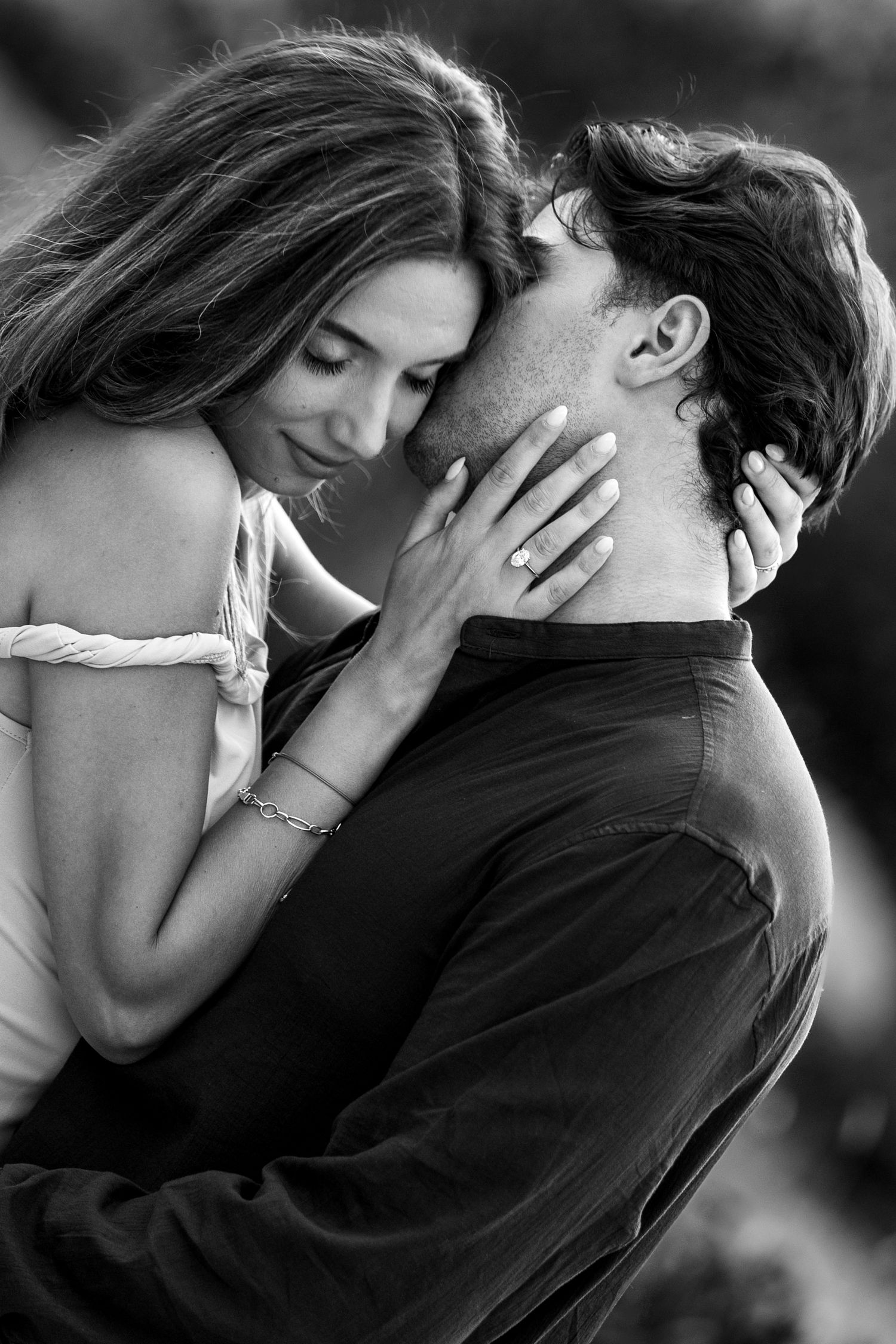 Black and white intimate portrait of couple embracing tenderly with woman showing engagement ring.