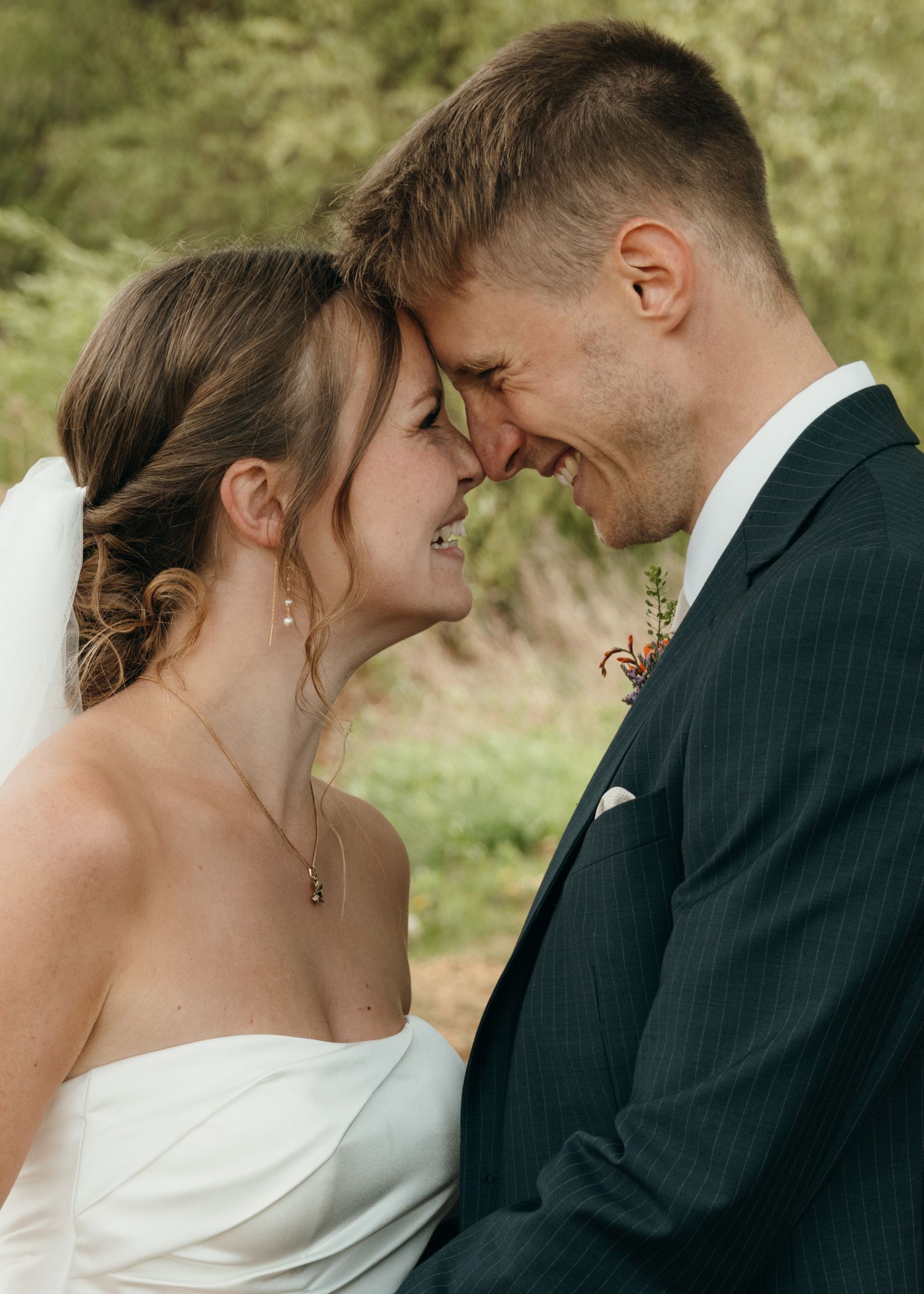 Bride and groom touch foreheads and smile affectionately in a close-up wedding portrait with a soft green background.