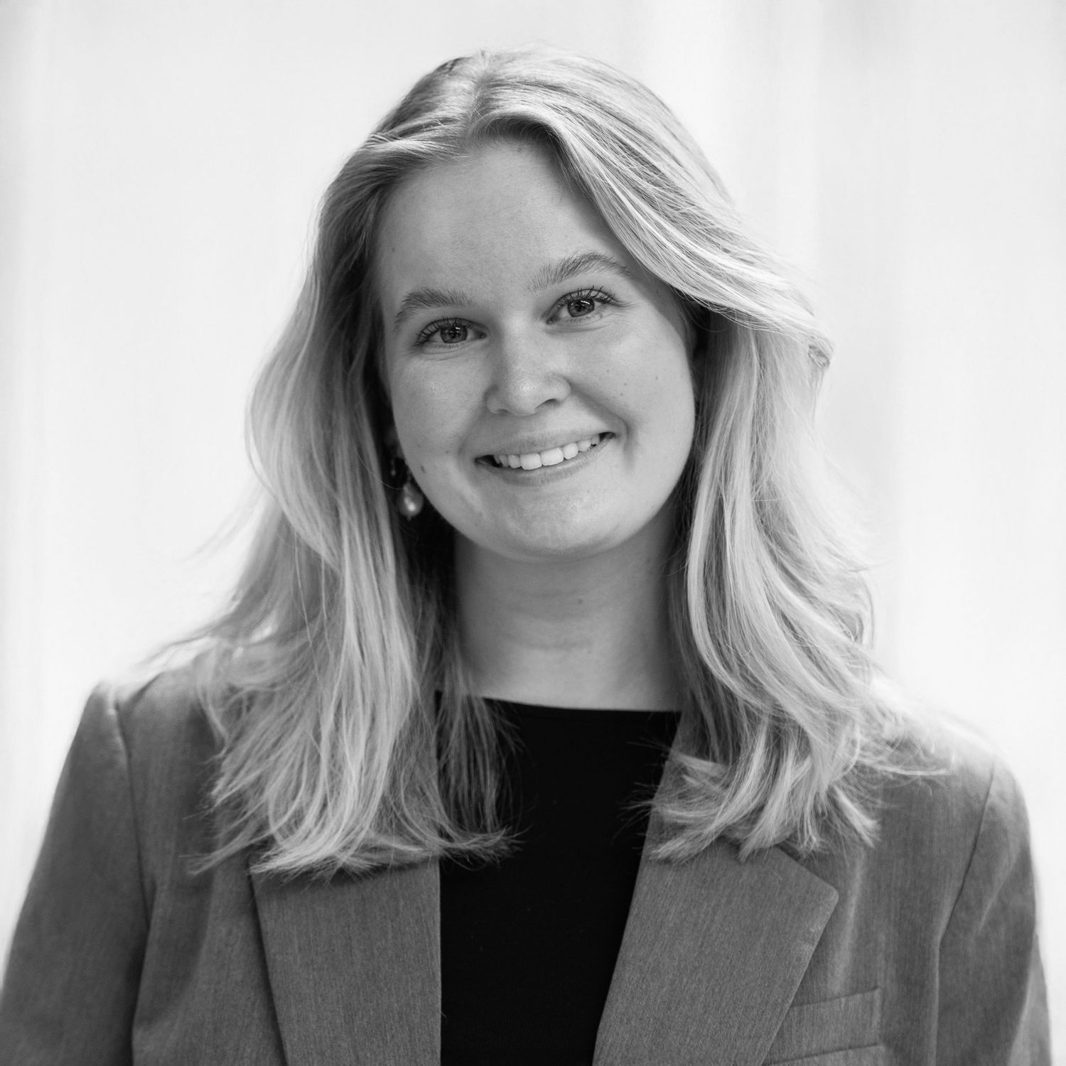 Black and white headshot of a smiling woman with long wavy blonde hair wearing a blazer over a dark top.