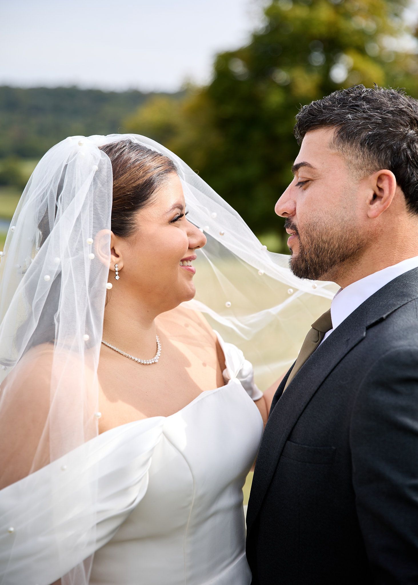 A bride and groom share a romantic moment outdoors, her white veil flowing as they gaze lovingly at each other.