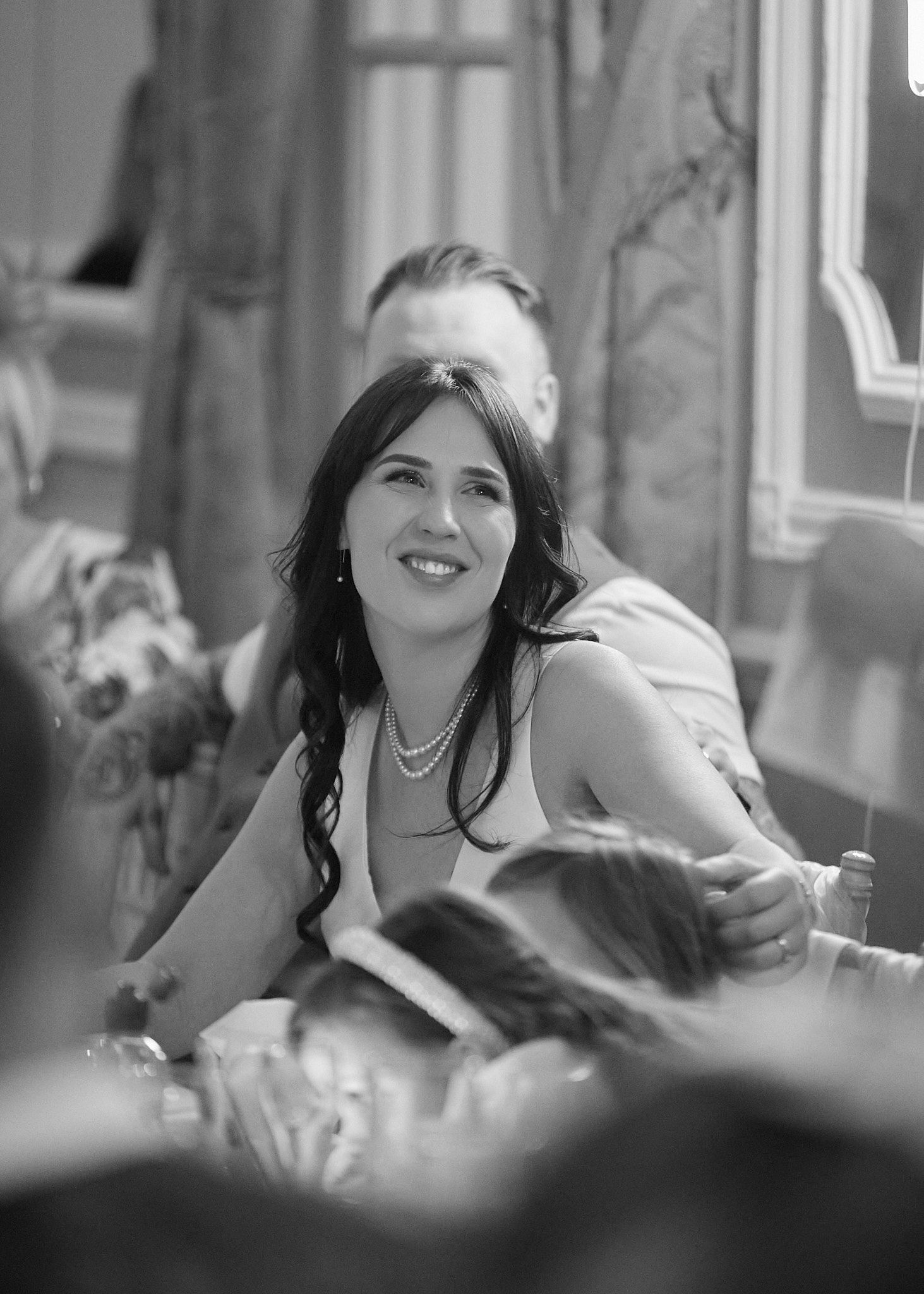 Black and white photo of a smiling woman with dark hair wearing a pearl necklace at a formal event. Ringwood hall wedding