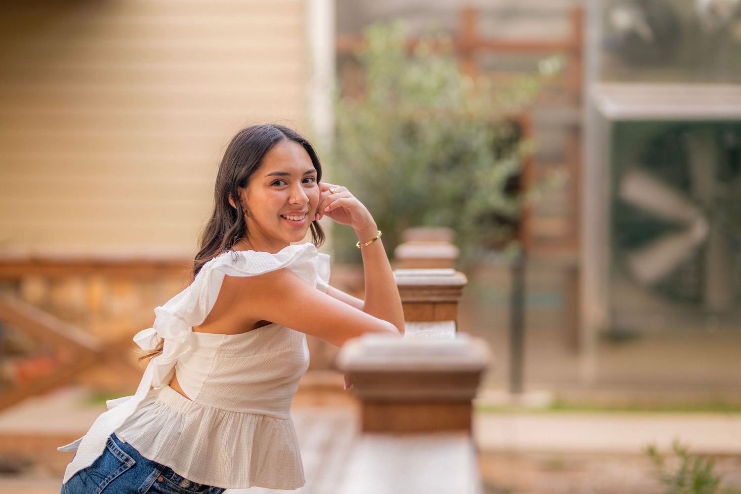 Young woman in white ruffled top and jeans smiling over shoulder outdoors in warm sunlight.