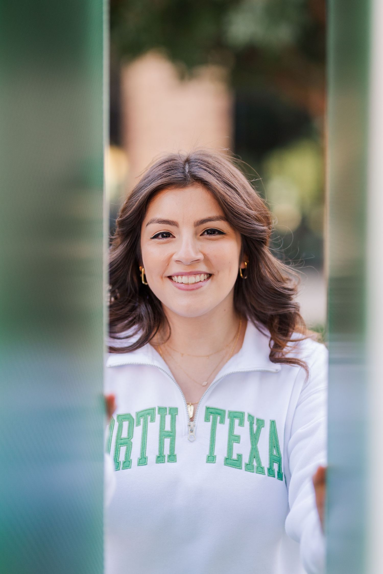 Smiling young woman in a white North Texas quarter-zip sweatshirt posing outdoors on campus.