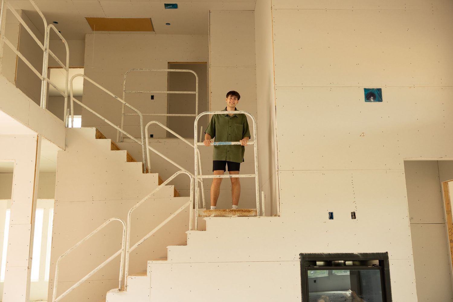 A young man in green shorts stands on white interior stairs with metal railings in a modern building.