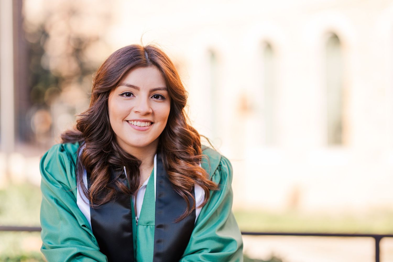 Young woman in green graduation gown smiling outdoors during graduation photo session.
