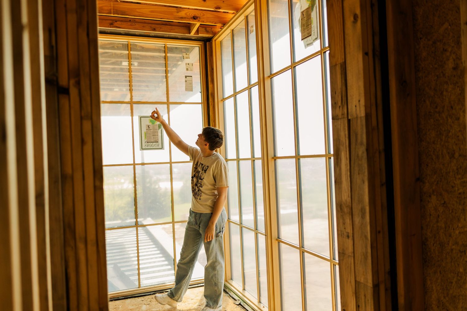 Person inspecting a glass French door in a wooden home under construction, reaching up to examine the frame.