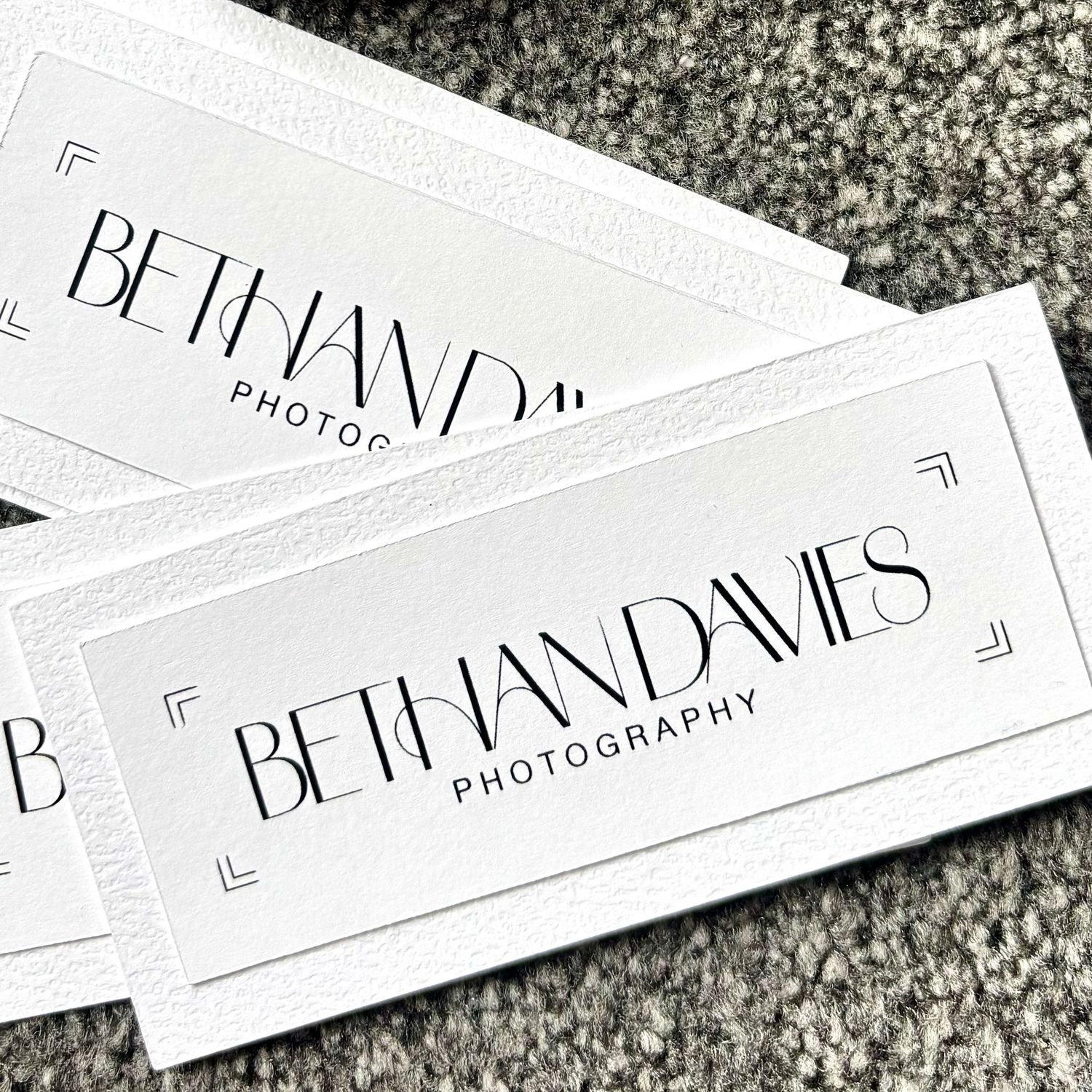 White business cards for Bethan Davies Photography featuring elegant Art Deco typography on a gray surface.