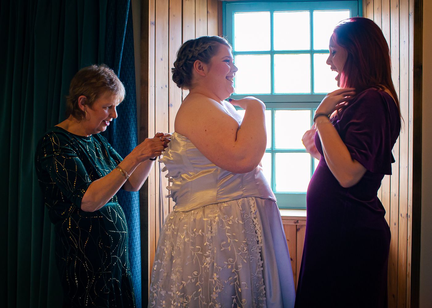 Two women help a bride in a blue and white gown with final dress adjustments before her wedding taken by Orkney Wedding Photographer