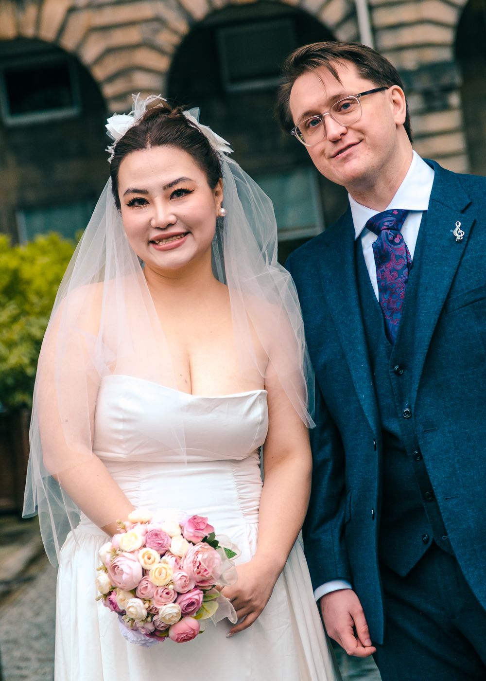 Smiling bride in white strapless gown with veil and groom in navy suit posing outdoors on wedding day taken by Orkney Photographer