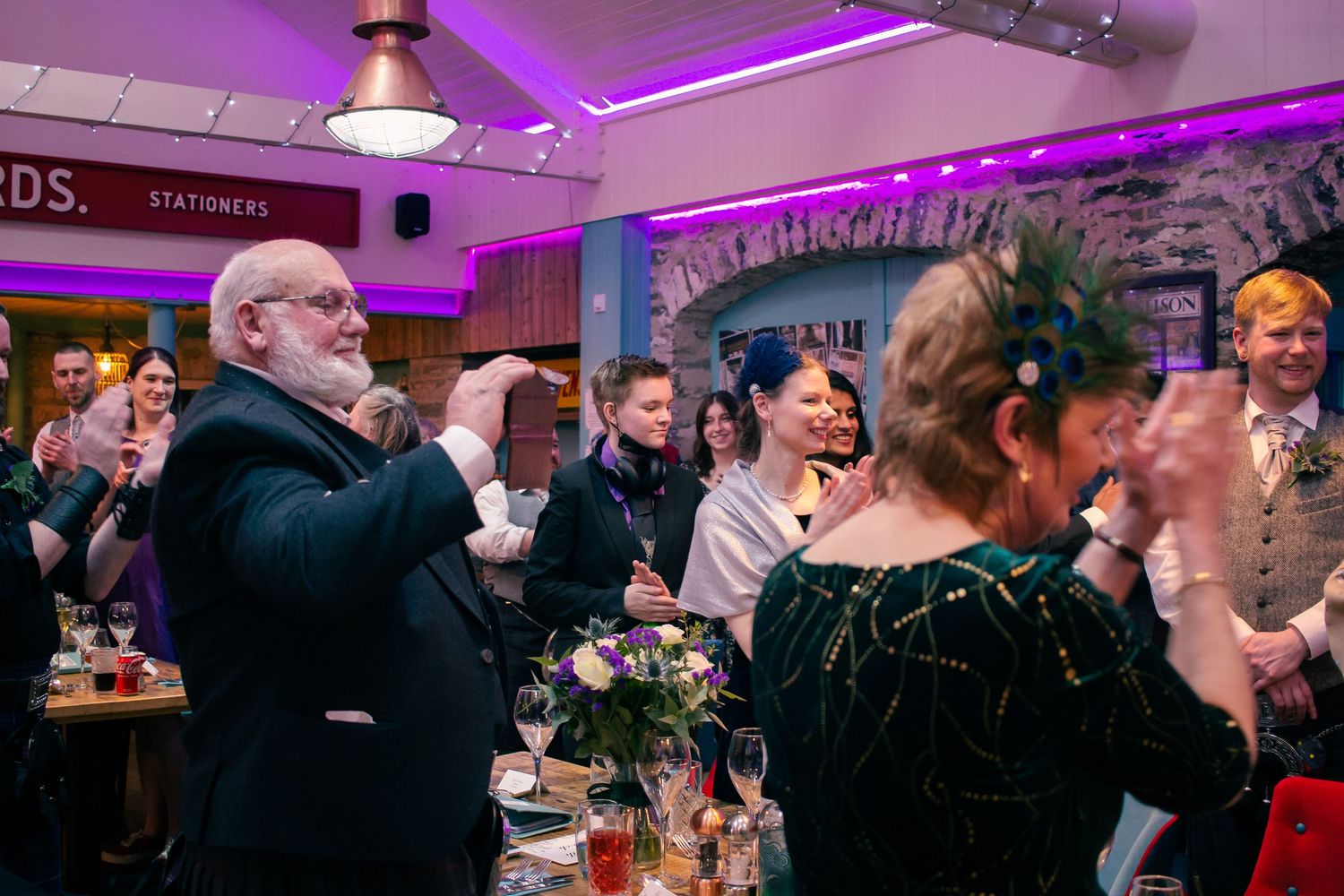 Guests clapping and celebrating at an elegant indoor wedding reception with purple lighting and decorative floral centerpieces in orkney.
