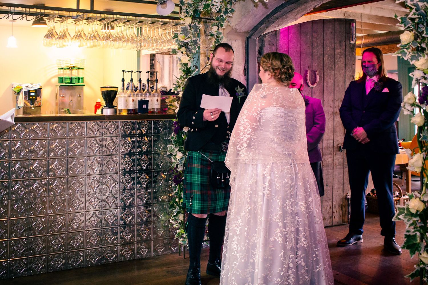 Groom in tartan kilt reads vows to bride in lace gown during indoor wedding ceremony at the storehouse, kirkwall.