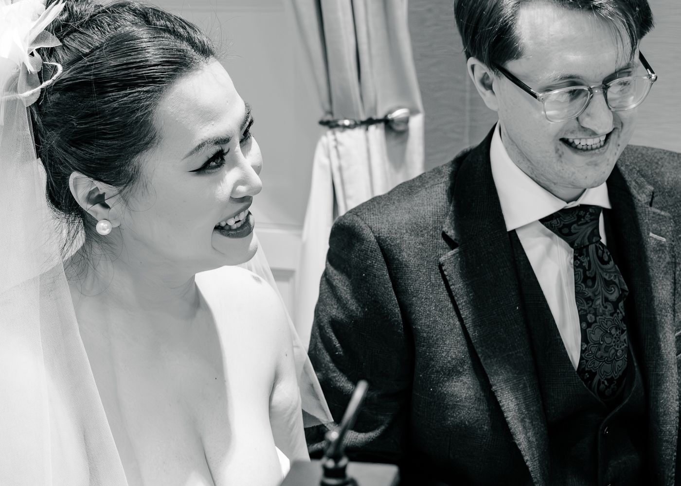 Black and white photo of smiling bride in veil and groom in suit during wedding ceremony taken by Orkney Photographer