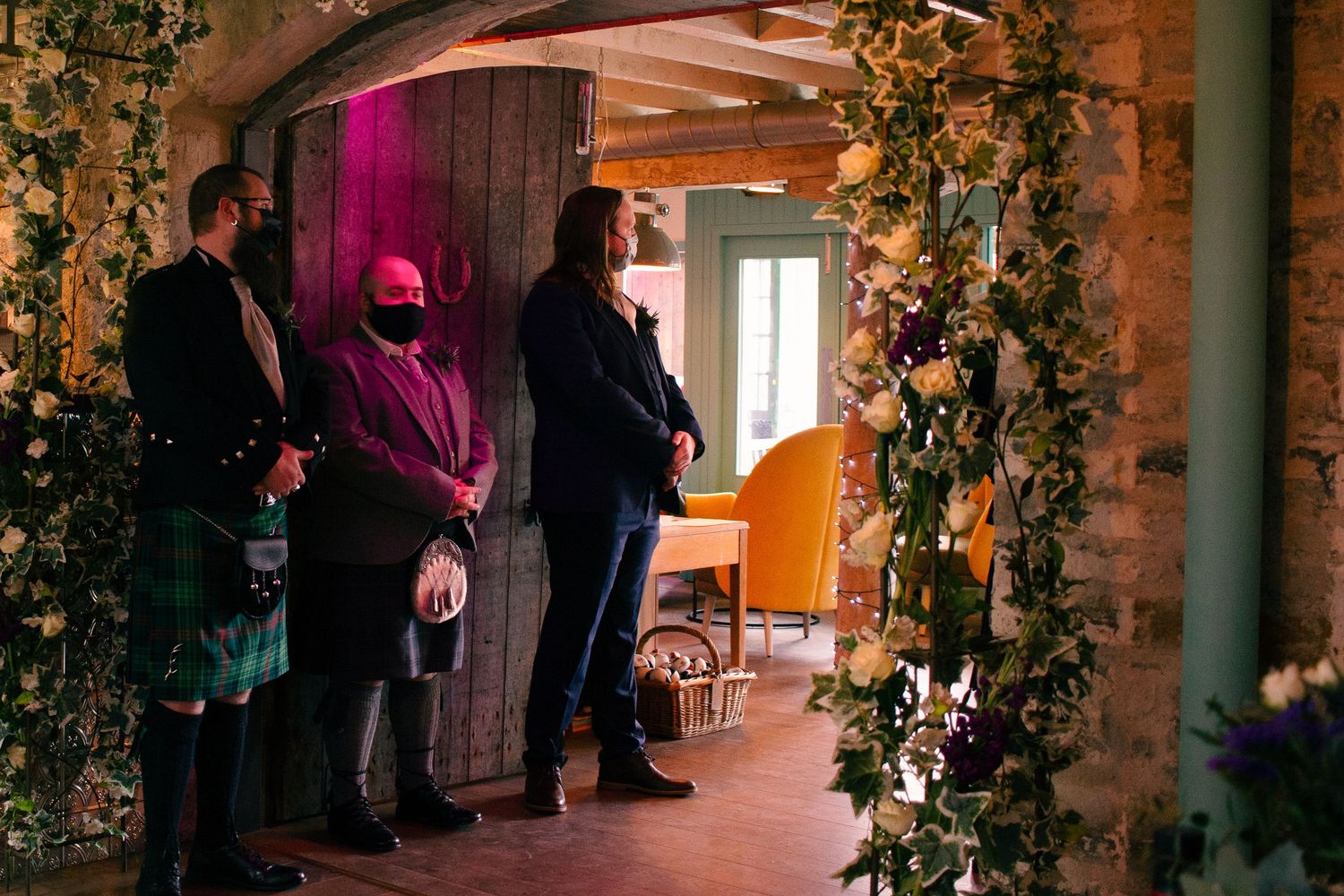 Guests in formal attire gather in a floral-decorated rustic venue corridor during an elegant wedding celebration at the storehouse, kirkwall