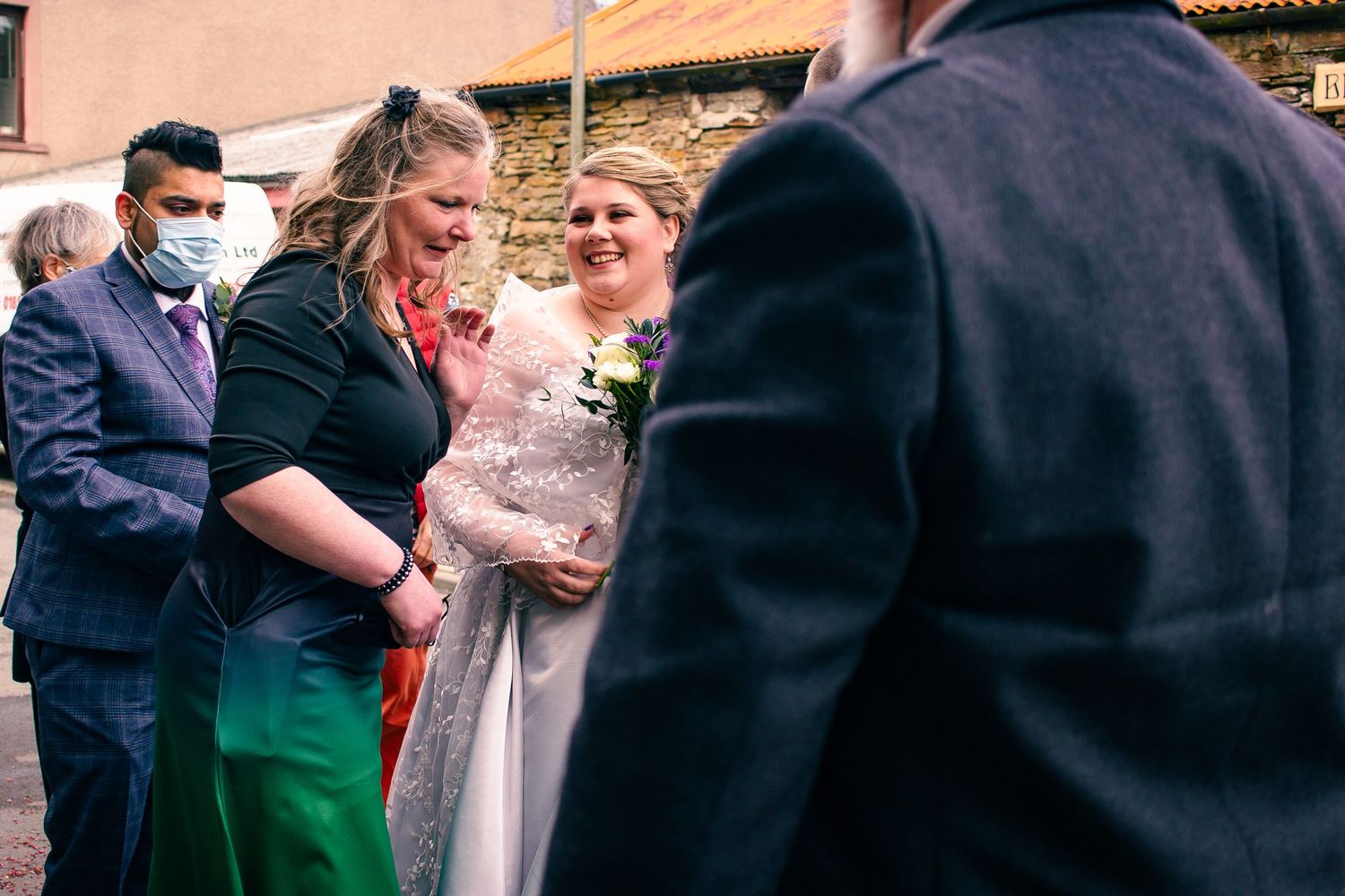 Two brides share a joyful moment with guests at an outdoor wedding celebration, one wearing a floral dress.