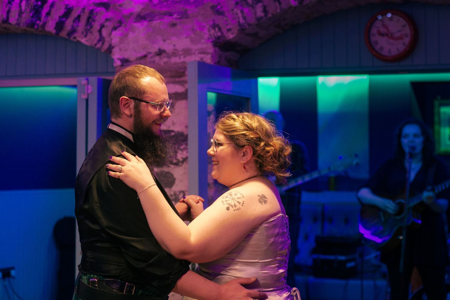 Couple sharing first dance at wedding reception with live guitarist performing in colorful purple and blue lighting at the storehouse,